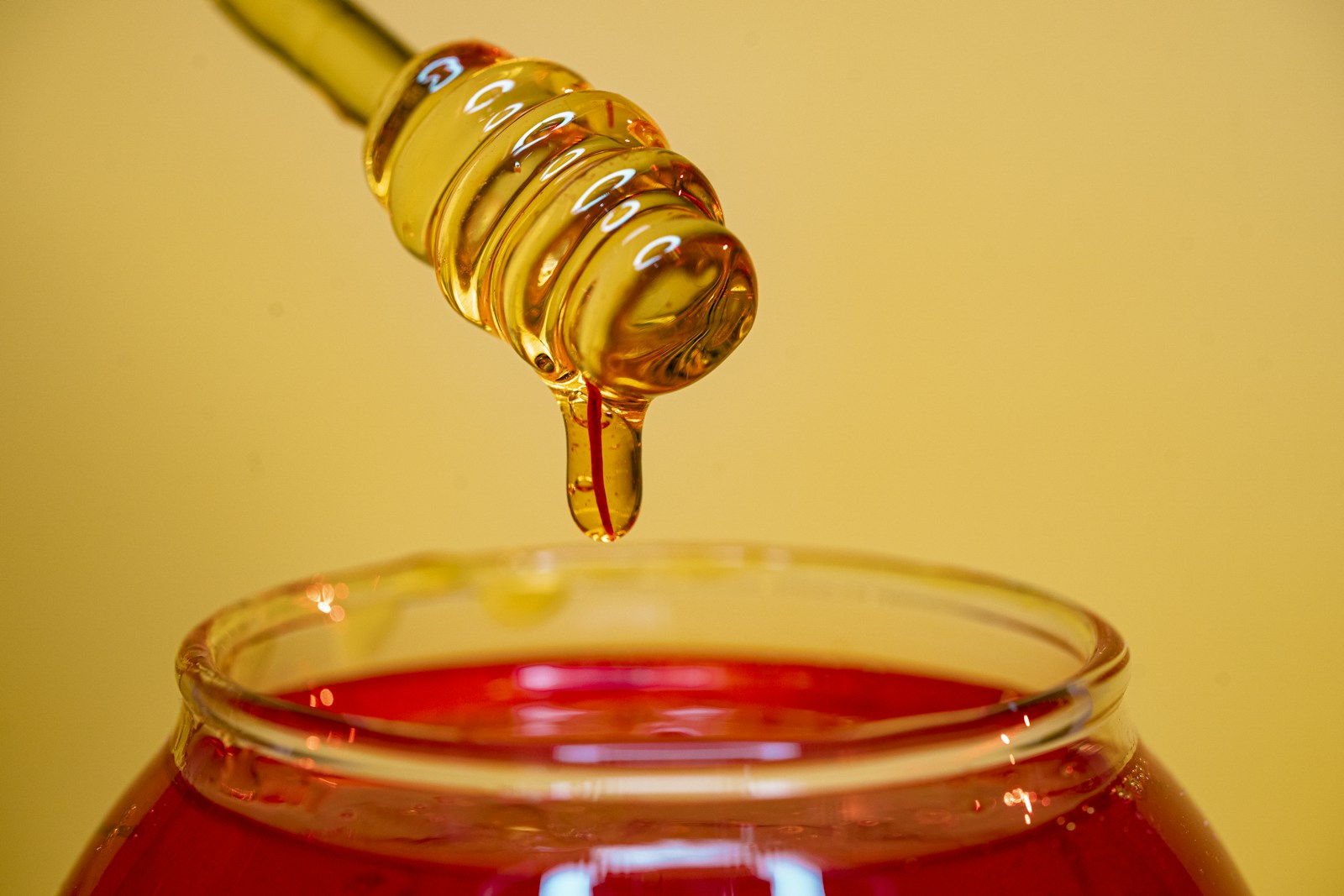 Honey dripping from a wooden dipper into a jar